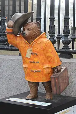 John Hurt's marmalade-themed Paddington Bear statue in London holding his hat up off his head.
