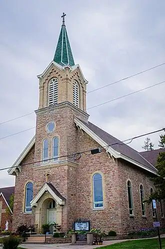 A small fieldstone church with a front-centered steeple constructed of bricks at the upper level
