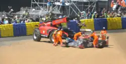 A race car being removed from the circuit after an accident by five people wearing orange for visibility