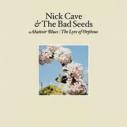 A photograph of a series of flowers in part of an arc are surrounded by a cream coloured border. Black text above the photograph reads "Nick Cave & The Bad Seeds" and italicised black text reads "Abattoir Blues / The Lyre of Orpheus".