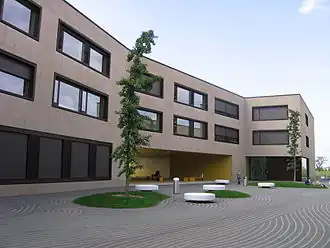 A modern, two-storey school building with a small tree in front of it.