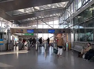 Turnstiles at Howard Beach-JFK Airport station. The station building has a high, sloped ceiling with glass skylights.