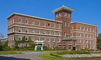 A brick building with two offset wings and a higher tower in the center with a peaked green top