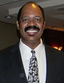An older African-American man smiling at the camera while wearing a tuxedo with a gray tie to go with his black and white colored tuxedo.