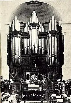 A picture of the interior of a church. A minister is standing in the pulpit in front of a large organ.