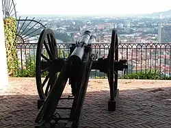 Photo shows an 18th century cannon overlooking a modern city.