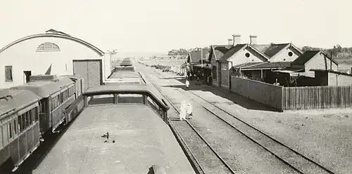 Photo of Beltana station building, goods shed and passenger train, taken by standing on the roof of one of the passenger cars