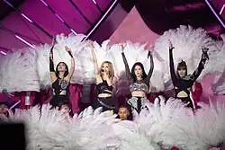 Blackpink with their hands raised, surrounded by feathers