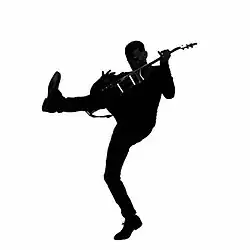 A black and white Silhouette of Bryan Adams playing his guitar with his left let up in the air.