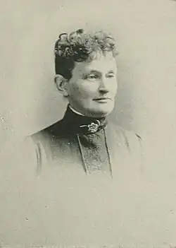 B&W portrait photo of a middle-aged woman with her hair in an up-do, wearing a high-collared blouse