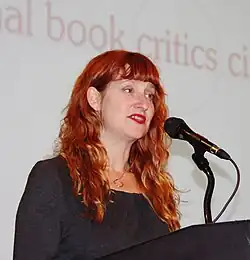 A woman with red hair speaks at a microphone
