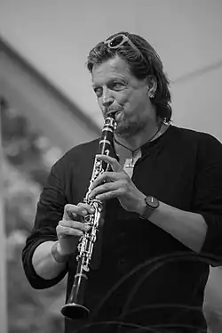 black and white photograph of a man with long hair playing a clarinet and looking to one side, probably on a stage