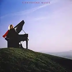 Cover of Christine McVie's 1984 album, showing McVie sitting behind a piano at the top of a green, grassy hill. She is looking to the right, toward the horizon, wearing a red scarf that is flowing in the opposite direction.