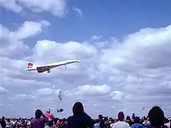 A BA Concorde, wheels and nose-cone lowered as if for landing, with a crowd of spectators in the foreground