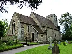 A photograph of a small church with a steep V-shaped roof and a square tower at the far end