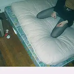 A person sitting on a mattress on the floor.