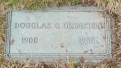 Flat bronze plaque in a cemetery, including him name, with birth and death years