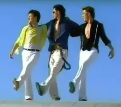 The three O-Zone members performing atop the wings of an airplane. They wear white pants and colored shirts—Todiraș and Balan with shirts open to the waist, accessorized with suspenders and sunglasses.