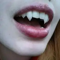 Close-up of a red-haired woman's mouth, opened to show her fangs