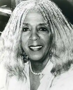 Ellen Stewart smiling, wearing a white shirt and pearl necklace