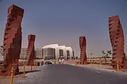 Four twisting red columns line a road leading to modern tan and white building.