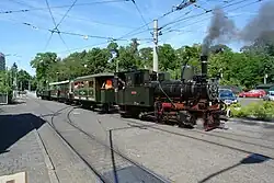 Steam locomotive with a train of four carriages running on tram lines in a section of street