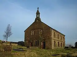 A two-storey stone church with round-headed windows and a bellcote on the near gable