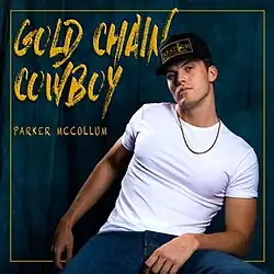 A man wearing a black-and-gold hat, gold chain necklace, white t-shirt, and blue jeans, sitting behind a blue curtain. The album title and artist's name appear on the left, colored in gold.