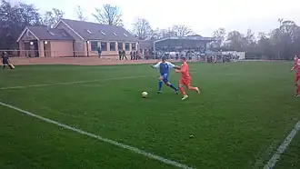 Hallam (in blue) on the attack in an NCEL match against Louth Town in 2014. The new clubhouse and main stand are in the background