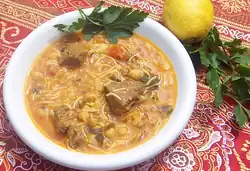 A bowl of light-coloured soup with meat, chickpeas and noodles