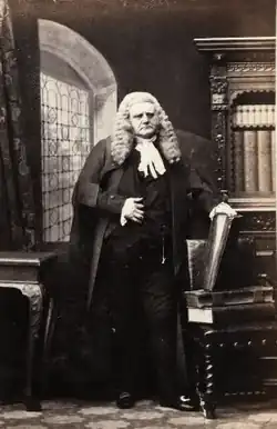 Standing portrait of Henry Bagshawe wearing judge's wig and formal dress, left hand on a vertical book