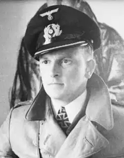 The head and shoulders of a young man, shown in semi-profile. He wears a greatcoat and his Iron Cross is visible at the front of his shirt collar. He wears a determined expression.