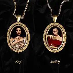 Two gold pendants lay over a sheet of wrinkled black velvet, containing photos of the two artists. The band's and album's names are written in cursive script underneath.