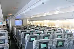 Interior view. Seats are separated by two aisles, in 3–4–3 configuration. A TV is positioned towards the front of aircraft.