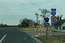 An intersection of a two-lane highway and another two-lane road in a rural area. Highway shields indicate both directions are County Route 1. A sign advises travelers to turn left (north) to reach Interstate 70, the Kansas Turnpike.