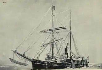 Two-masted sail-and-steam ship, with pennant flying from topmast, sails furled, lying stationary in a frozen sea