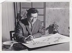 Kazuo Hamasaki sits at his desk painting chickadees in the Japanese sumi-e style