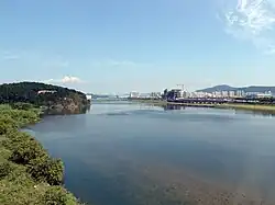 A vast and tranquil river in a clear day of fall. Apartment blocks and buildings under construction are seen at a distance.