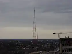 At dusk, a silhouetted, unlit TV tower looms over the Kansas City skyline as seen from the air.