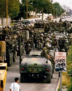 Many soldiers and military vehicles near a vandalized road sign