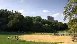 People on a playing field with trees and high-rise buildings visible in the background