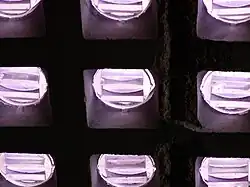 View from below of small circular panes of translucent lavender glass, deeply set in a coffered grid. Each circle has three parallel pendant-prism ridges.
