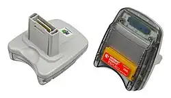 An image of the front and back of the Japanese 64GB Pack accessory. The front is made of light gray plastic and has a large protruding plastic plug with electronic connectors. The back is made of translucent dark gray plastic with a receptacle slot for a Game Boy game cartridge to slide in parallel to the back. A thin red sticker on the back displays the device's name, model number, and assorted legal indica.
