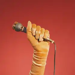 A yellow gloved hand holds a brass microphone amongst a red gradient background.
