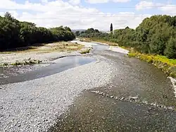 a gravel river is seen meandering through bush and trees on either bank