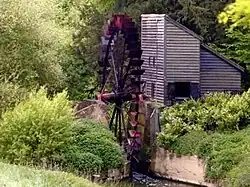 A colour photograph of a red undershot waterwheel connected to a timber-clad building