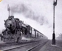 An old black and white photo of a steam locomotive pulling a fast passenger train