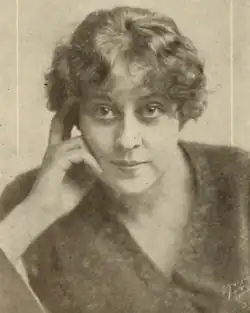 A white woman with light wavy hair, face resting on one hand