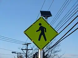 A pedestrian crossing sign in the United States with solar-powered lit outline