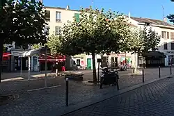 Photograph of a shaded square with houses in the background.